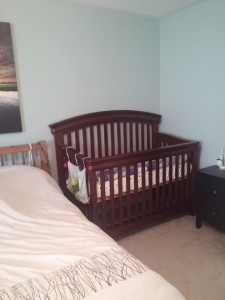 Small nightstand with diapers and sleepers. Crib set up beside the bed.